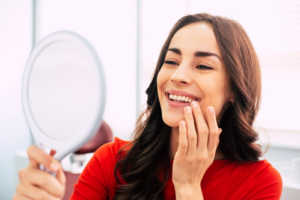 Woman checking her smile in the mirror and loving her dental implants